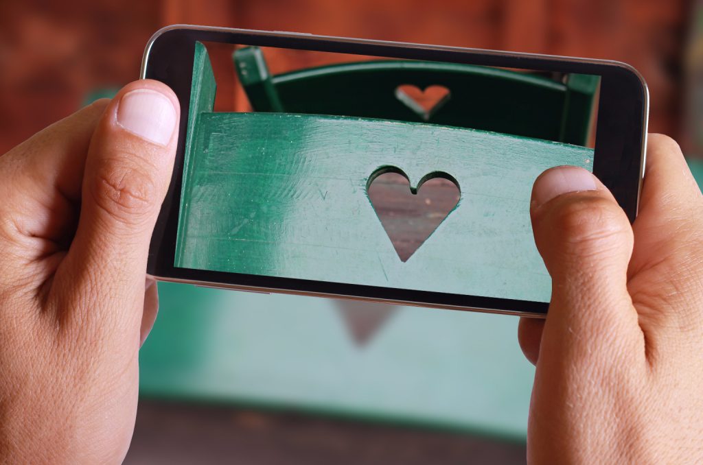 Male hand taking photo of Love concept, two wooden chairs decorated with heart shape. Happy valentine's day background with cell, mobile phone.
